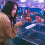 Woman observing goldfish in a tank equipped with blue aquarium circulation pumps, illustrating pump use for healthy water flow.