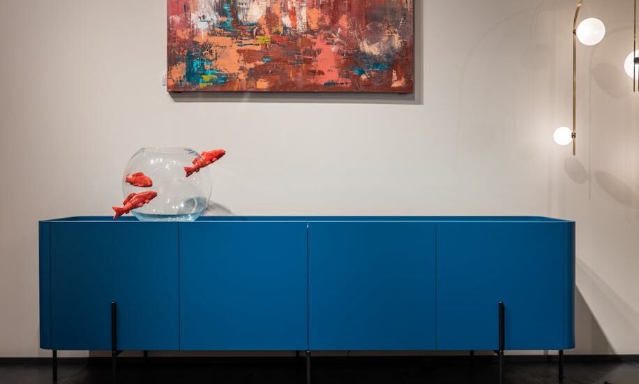 aquarium stand with fish tank — Modern blue cupboard with glass aquarium decorated with fish placed at white wall with creative picture in modern room with glowing lamps