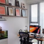 A planted aquarium with a visible surface skimmer sits beside a computer desk in a bright, modern home office setup.