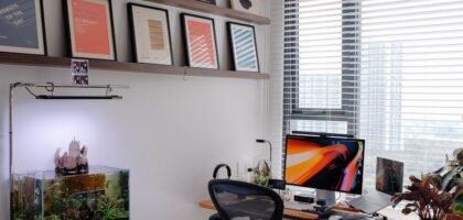 A planted aquarium with a visible surface skimmer sits beside a computer desk in a bright, modern home office setup.