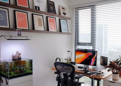 A planted aquarium with a visible surface skimmer sits beside a computer desk in a bright, modern home office setup.