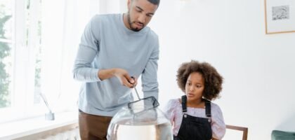 Man cleaning a round fish bowl with a net while a child watches, illustrating aquarium gravel vacuum care tips.