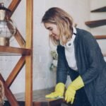 A woman in yellow gloves cleans a wooden shelf, relating to maintaining a healthy aquarium environment with fertilizers.