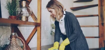 A woman in yellow gloves cleans a wooden shelf, relating to maintaining a healthy aquarium environment with fertilizers.
