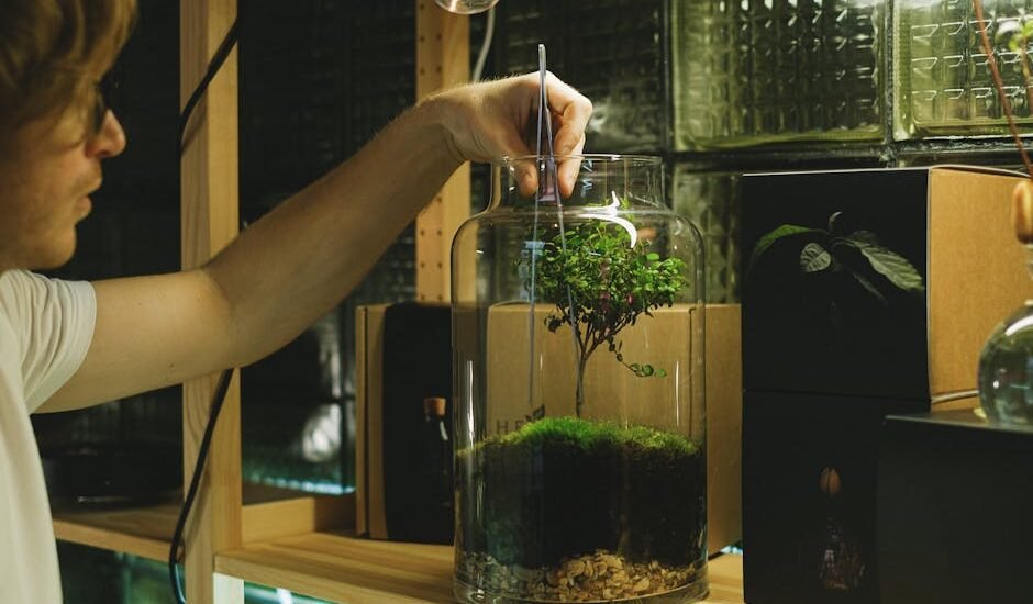A man uses tweezers to tend a moss terrarium, showcasing a hobbyist's attention to detail indoors.