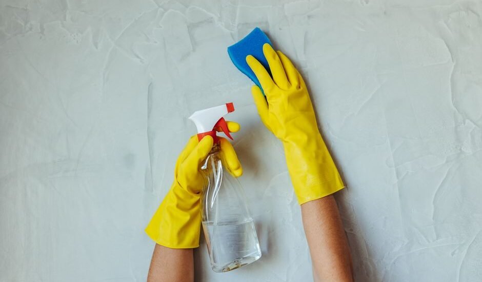 Hands in yellow gloves using a spray bottle and sponge for cleaning, relevant for aquarium air stones maintenance.