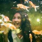 A woman smiles while observing goldfish in an aquarium, relating to auto top off systems.