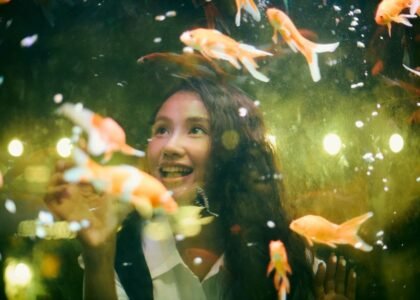 A woman smiles while observing goldfish in an aquarium, relating to auto top off systems.