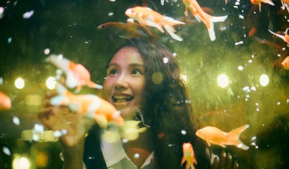 A woman smiles while observing goldfish in an aquarium, relating to auto top off systems.