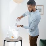 A man adds water to a frameless aquarium on a stand, showcasing modern design.